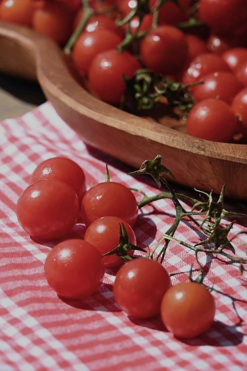 A close-up shot shows several bright red San Marzano tomatoes, some still on the vine, with green leaves and a blurred background.