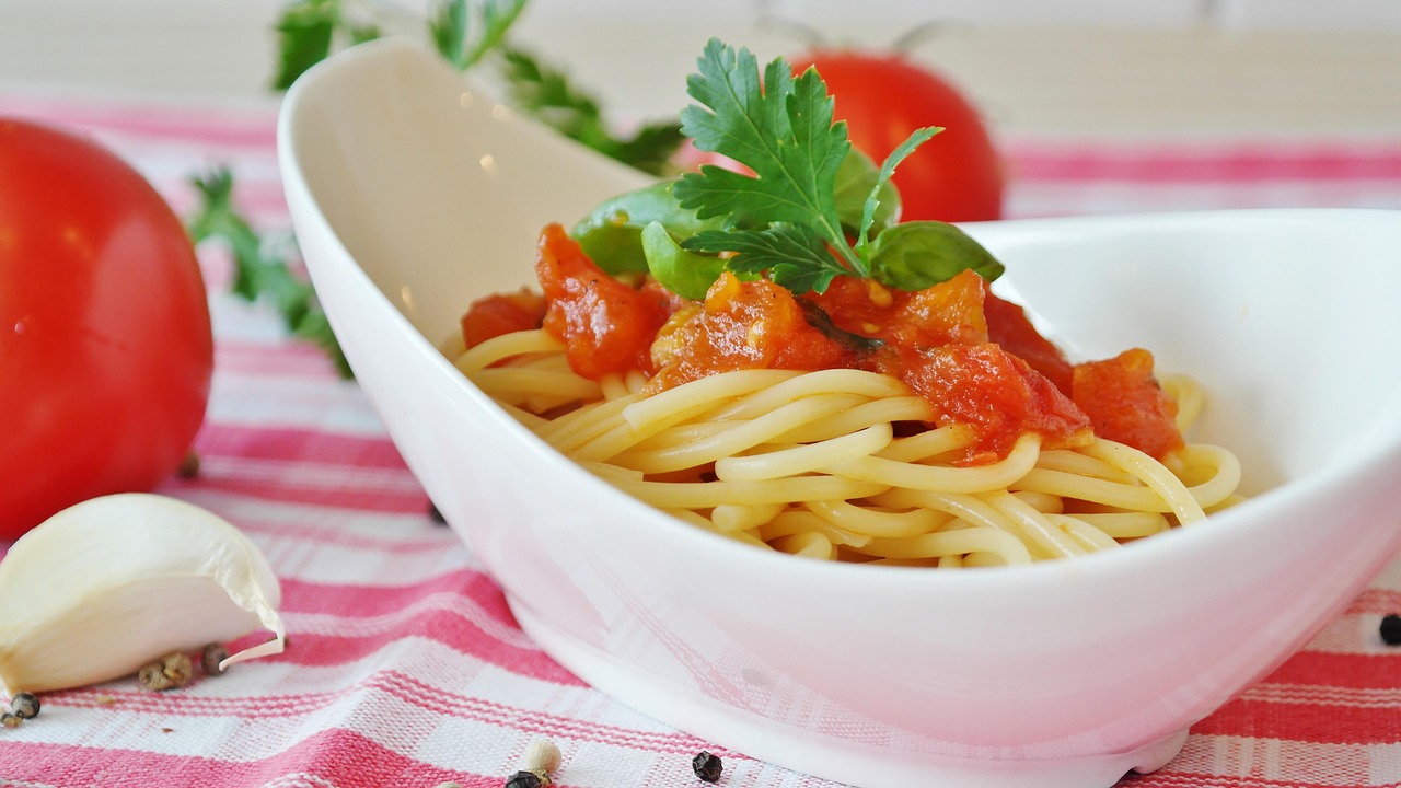 A close-up shot shows several ripe San Marzano tomatoes, characterized by their elongated shape and vibrant red color, hanging from a vine in a garden.