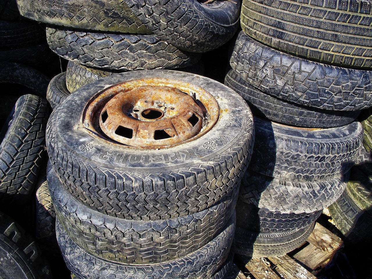 A stack of four car tires is shown in a garage or storage area, with a white wall and a window in the background.