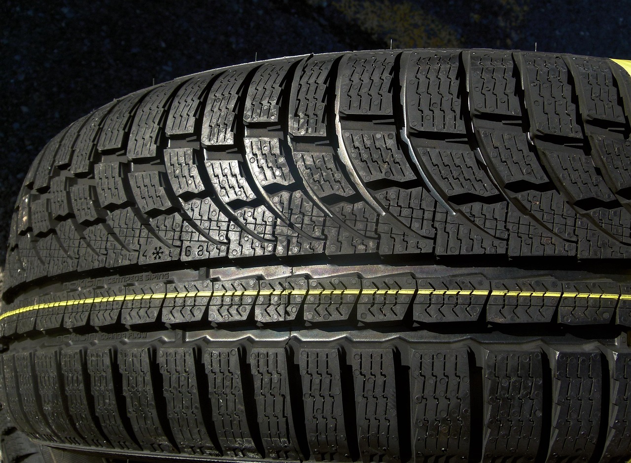 A close-up shot shows a person's hand holding a tire tread depth gauge against a worn car tire, indicating a low tread depth.