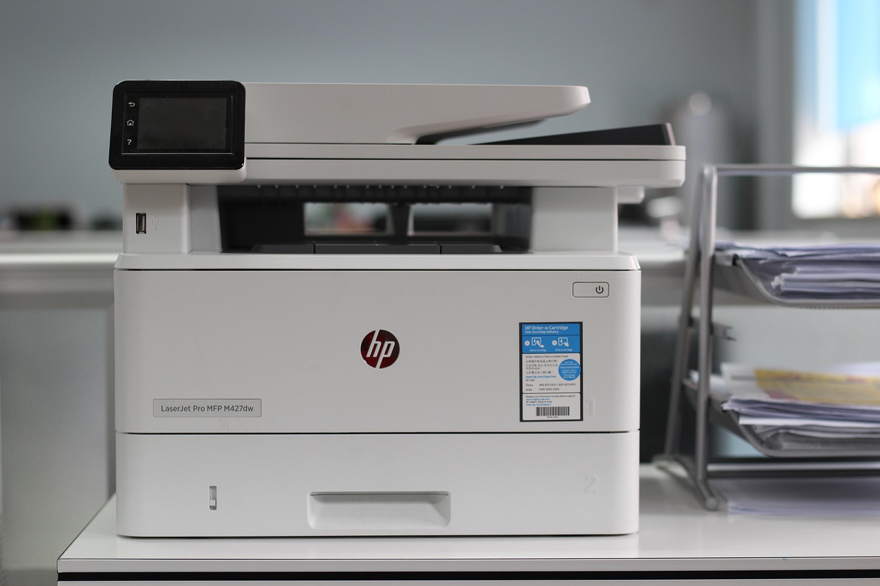 A close-up shot shows the control panel and paper tray of a modern office printer or copier, with a hand reaching towards the buttons.