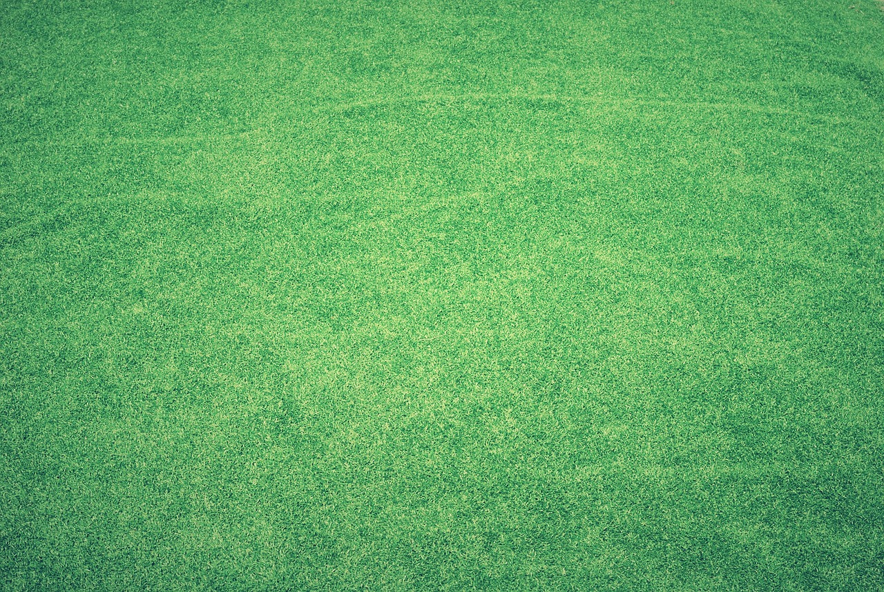 A person is installing a roll of turf on a patch of dirt, carefully unrolling it to cover the ground.
