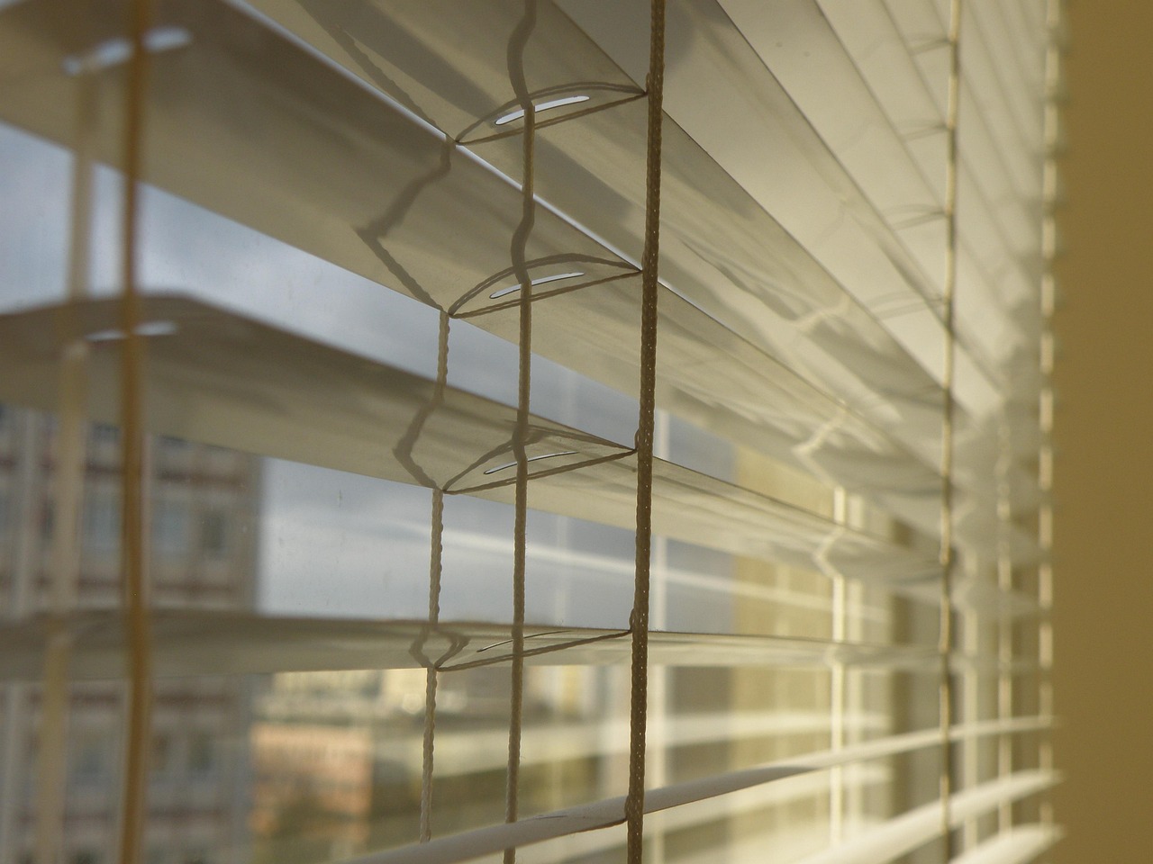 A person is installing a white Venetian blind on a window, with a drill in hand and tools scattered on the windowsill.