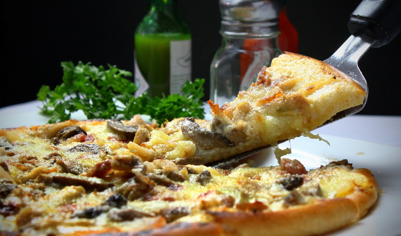A close-up shot shows a slice of pizza being lifted from a whole pizza, with visible toppings including cheese, pepperoni, and green peppers.