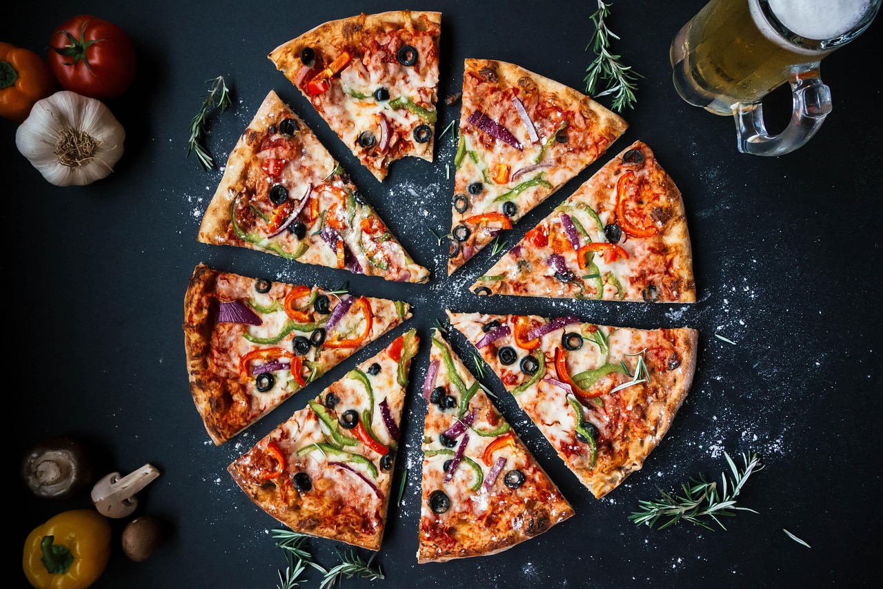 A close-up shot shows a slice of pizza being lifted from a whole pizza, with visible toppings including cheese, pepperoni, and green peppers.