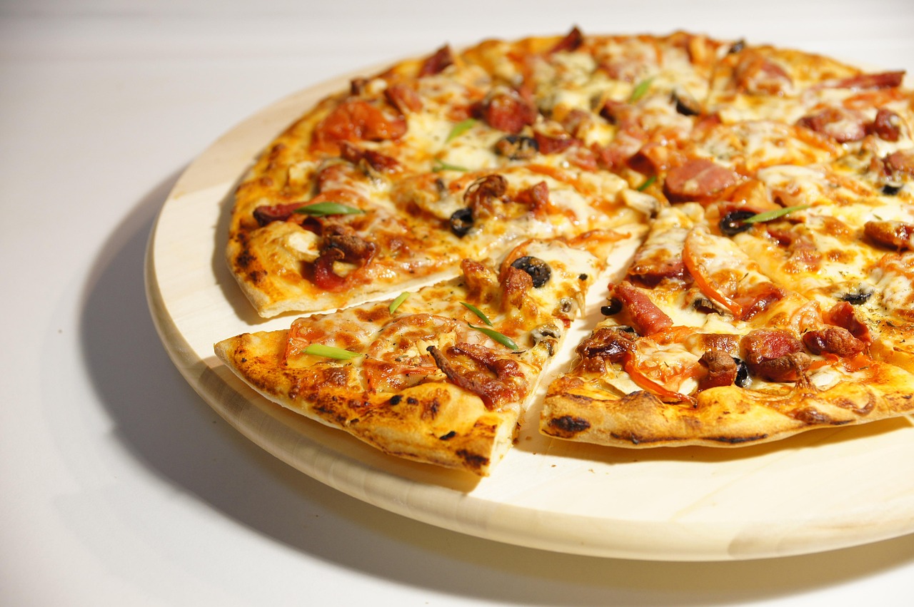 A close-up shot shows a hand stretching a piece of raw pizza dough, revealing its elasticity and texture.