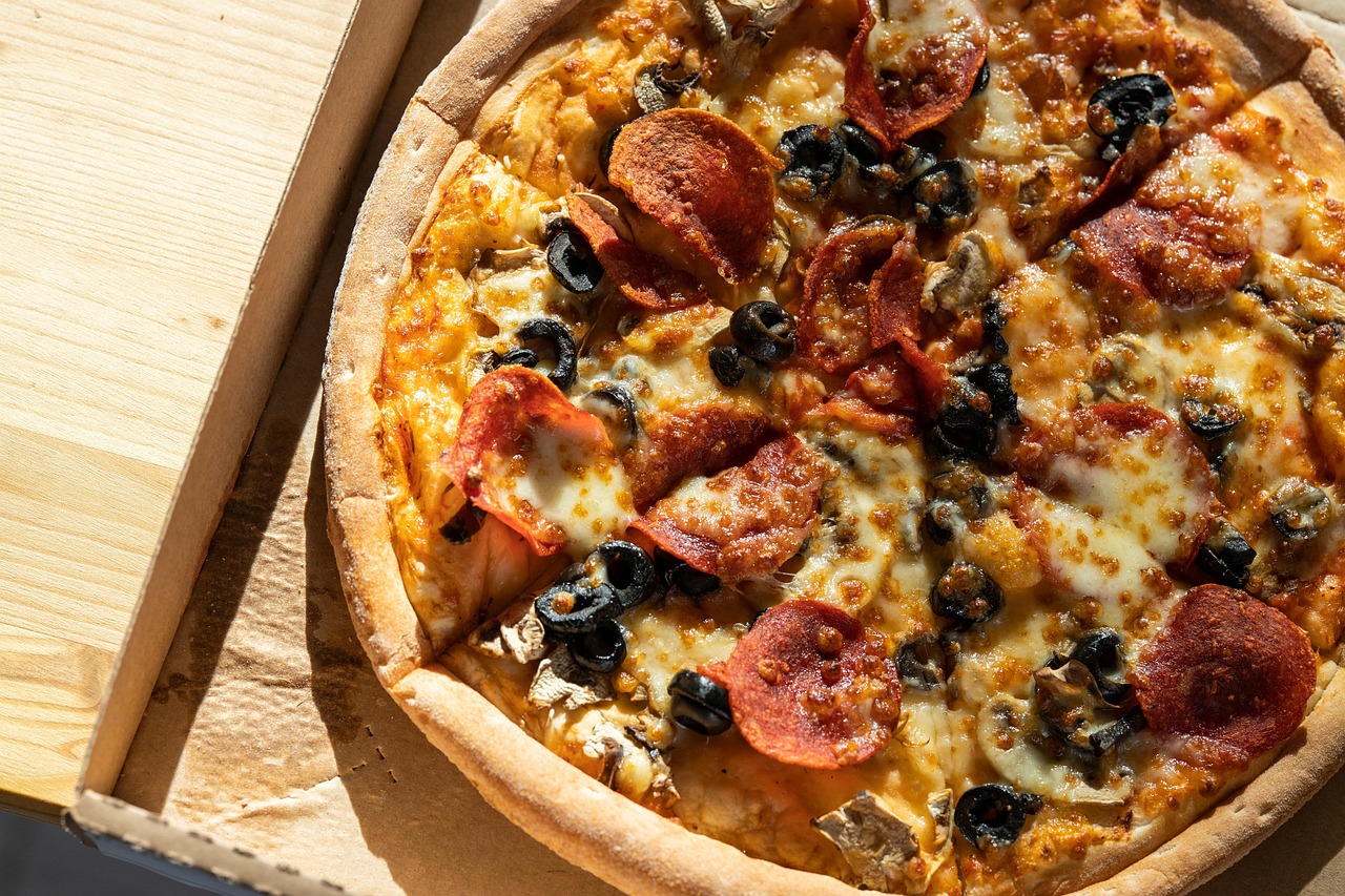 A close-up shot shows a person's hands stretching and kneading a large, round piece of pizza dough on a floured wooden surface.