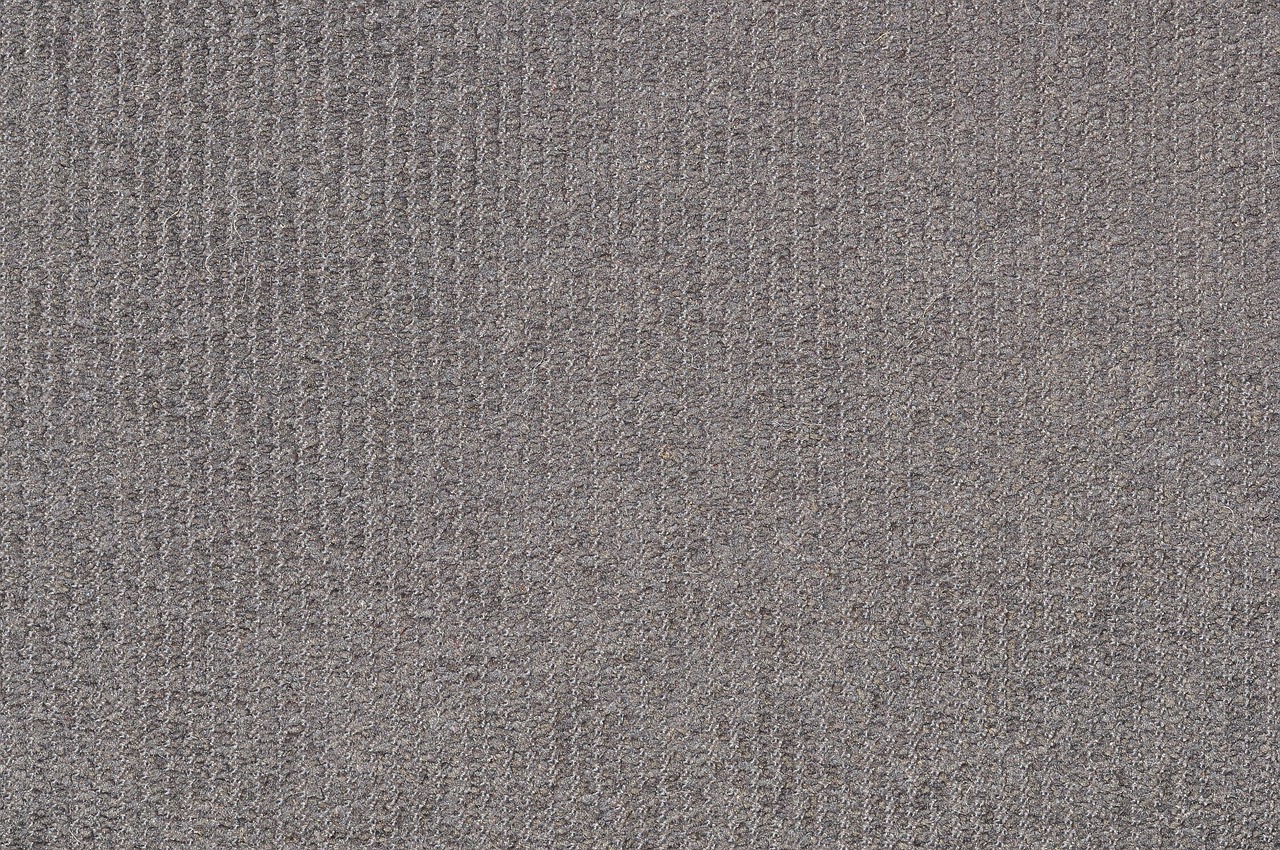 A person is using a vacuum cleaner to clean a patterned rug in a room with wooden flooring.