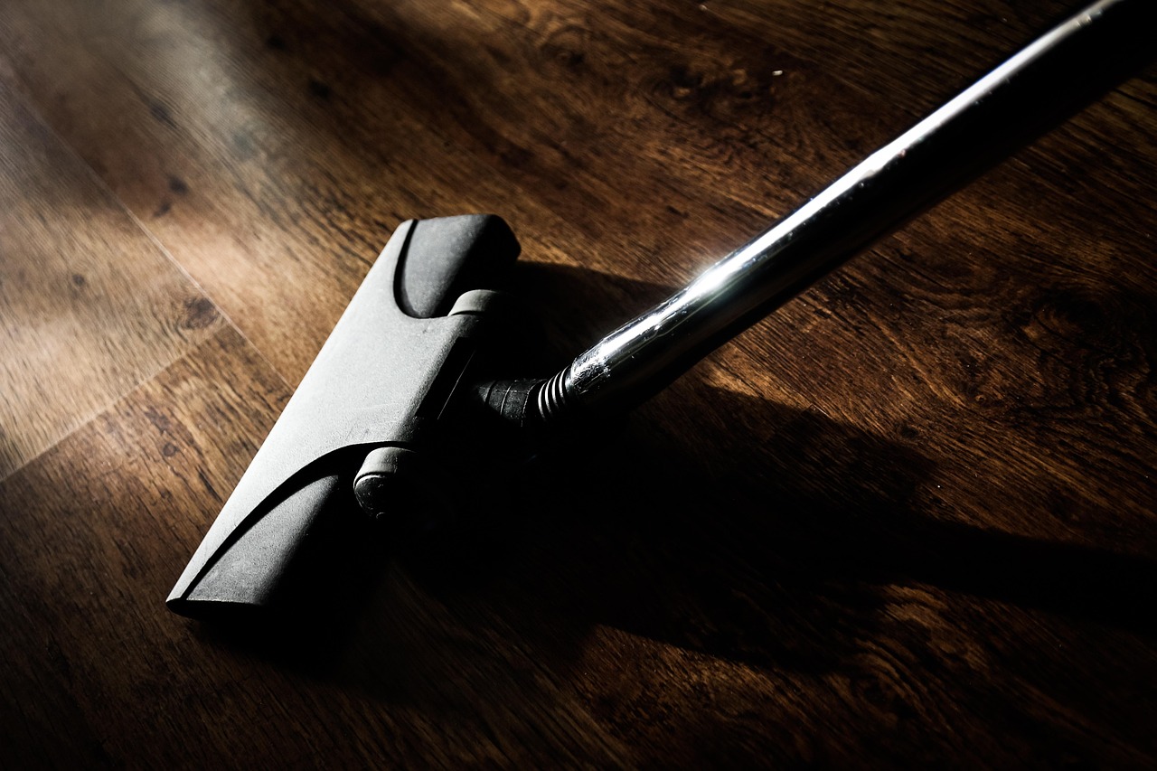 A person is using a vacuum cleaner to clean a patterned rug in a room with wooden flooring.