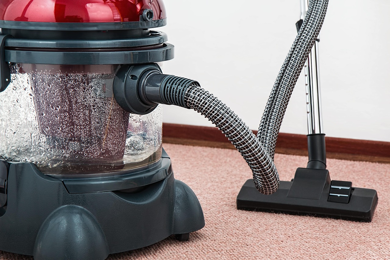 A person is using a vacuum cleaner to clean a shaggy, light-colored rug or carpet.