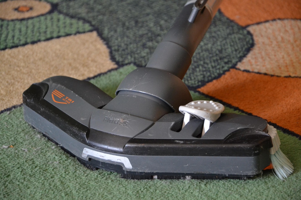 A person is using a vacuum cleaner to clean a shaggy, light-colored rug in a room with wooden flooring.